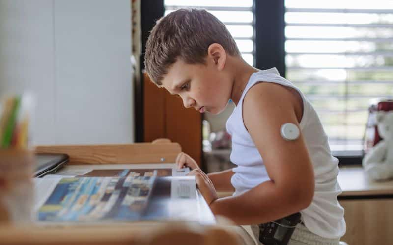 A diabetic boy is shown doing homework while wearing a closed loop insulin pump system.